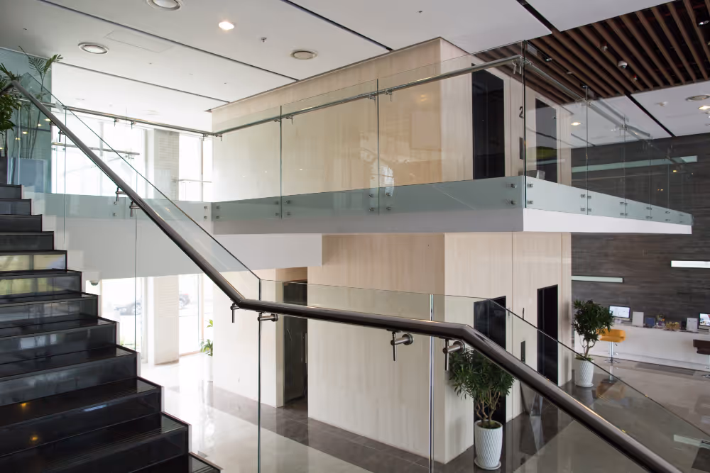 Escada preta moderna com corrimão de metal e vidro em um ambiente corporativo com plantas e balcão de recepção.